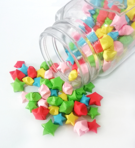 A glass jar tipped over with origami stars spilling out.