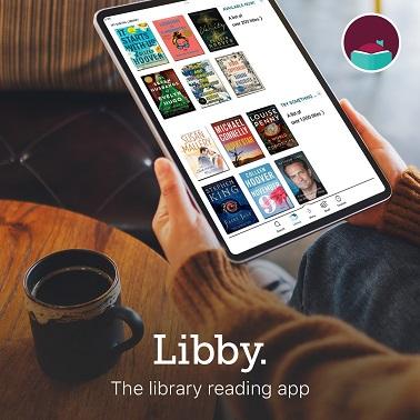 Hands holding a tablet that displays book covers in the Libby App. Person is at a table with a mug. Text at the bottom says "Libby The Library Reading App"